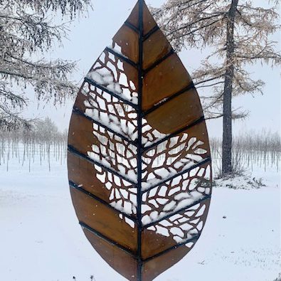 An outdoor sculpture of a large metal leaf, with it's skeleton veining spreading from one side to the other.