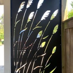 A black privacy panel with an illustration of grasses cut from it. It separates the driveway from the backyard.
