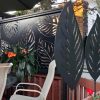 The installed high privacy screen, with a modern leaf design cut into the metal panel. Three leaf sculptures are paired with the panel.