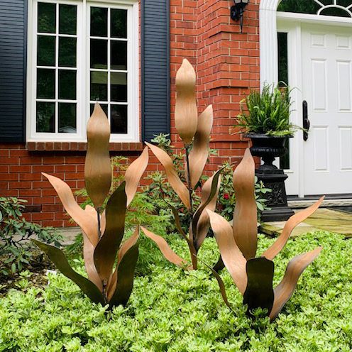 Three flora sculptures stand in a garden, in front of a lovely Ontario home.